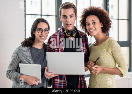 Giovani allegro team di tre persone a guardare un video o cerca su una presentazione aziendale su laptop in ufficio Foto Stock