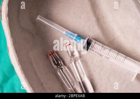 Siringa medica e fiale giacente in una capsula in ospedale è sfondo verde. Lo sfondo può essere una parte di tessili di un medico o un infermiere's w Foto Stock