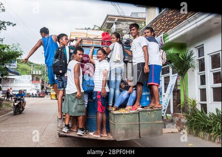 Un gruppo di filippini locali si aggrappano sul retro di un autobus mentre si accelera nella città di El Nido, Palawan, Filippine. Foto Stock