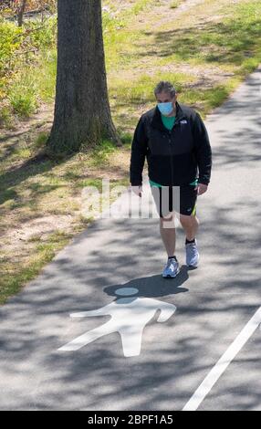 Un uomo che indossa una maschera chirurgica, fare passeggiate, su un percorso vicino alla Marina Bayside a Queens, New York City Foto Stock