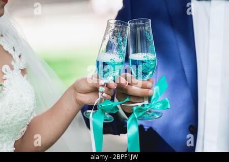 splendida bride e sposo con champagne, mattina del matrimonio. mani con eleganti bicchieri di vino blu Foto Stock