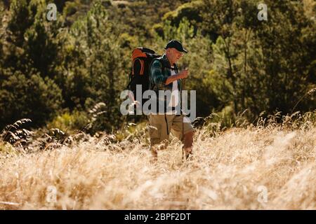 Uomo anziano che cammina su un sentiero di montagna. Uomo maturo che porta uno zaino trekking in natura. Foto Stock