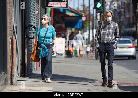 Le persone che indossano maschere facciali passano davanti a negozi chiusi ad Haringey, Londra, dopo l'introduzione di misure per portare il paese fuori dalla zona di blocco. Foto Stock