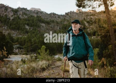 Uomo anziano che cammina su un sentiero di montagna. Uomo maturo sicuro che porta uno zaino escursioni in natura. Foto Stock