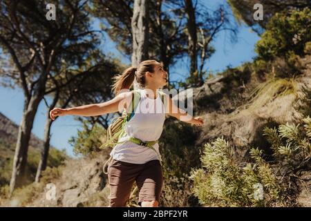 Donna eccitata che corre con le braccia distese su un sentiero di montagna. Donna in viaggio di trekking cercando eccitato. Foto Stock