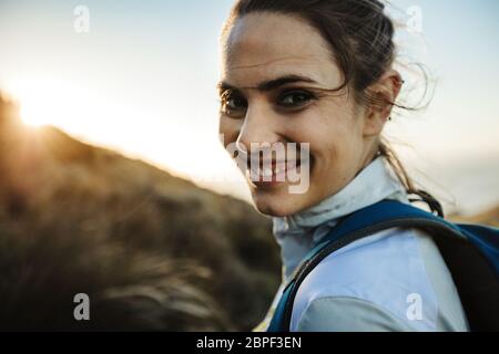 Primo piano di una donna sorridente escursionista in montagna. Donna alpinista che arrampica una montagna guardando la macchina fotografica e sorridendo. Foto Stock