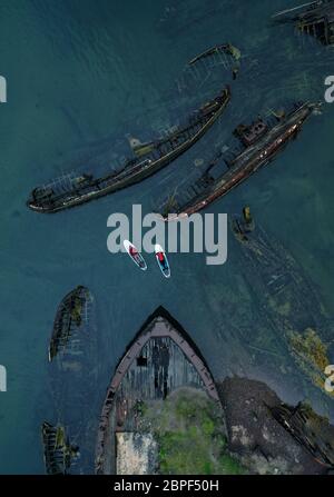 Uomo e donna sulle tavole SUP nel cimitero delle navi. Vista aerea. Teriberka, Penisola di Kola, Russia. Foto Stock