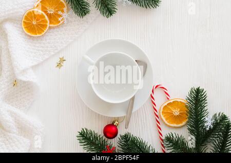 Composizione di natale con decorazioni. Bianco vuoto cup, sciarpa lavorata a maglia e di Abete rami su un bianco tavolo in legno prima di natale. Foto Stock