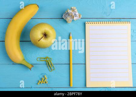 Aprire il notebook e frutta fresca su di un legno blu scrivania in ufficio. Piano immagine di laici con il giallo delle forniture per ufficio e prima colazione Foto Stock