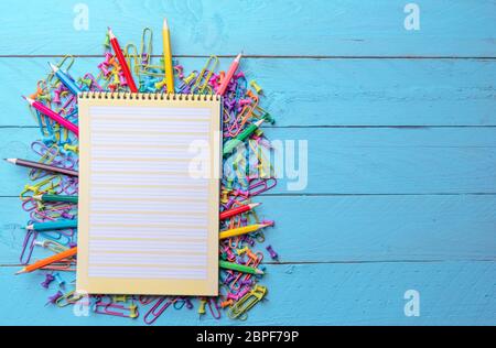 Pagina vuota per notebook a spirale su una pila di forniture per ufficio, carta colorata morsetti, spingere i perni e le matite di legno. Foto Stock