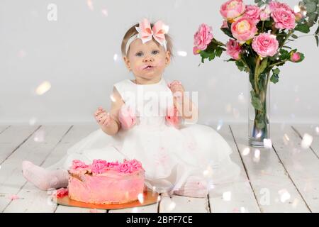 Un bambino di un anno con una torta di compleanno. Divertente bambina sbavata di crema il suo compleanno. Bambino divertente in vacanza. Ragazza carina con pastri rosa Foto Stock