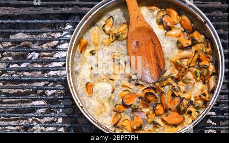 Purificati da conchiglie di mare cozze cuocere in una salsa cremosa su un fuoco aperto all'esterno. Foto Stock