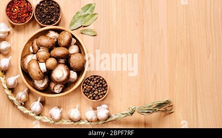Funghi in piastra di legno, treccia di aglio, allspezia e foglie di alloro su una superficie di legno chiaro. Vista dall'alto. Foto Stock