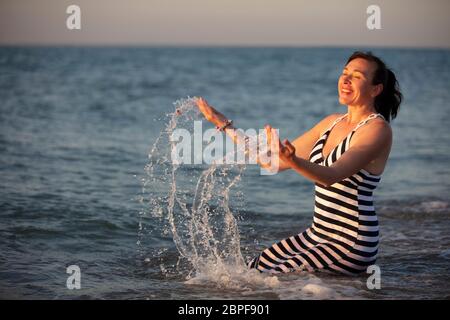 Riposatevi al resort. Donna anziana in vacanza al mare con spruzzi di acqua.acqua di mare di guarigione. Foto Stock