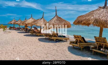 Turismo sull'isola di Gili Air in Indonesia, con una fila di ombrelloni e mobili di bambù in paglia per i turisti su una spiaggia di sabbia bianca. Foto Stock