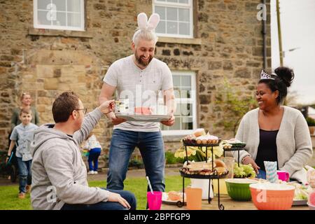 Metà uomo adulto che porta un vassoio con tazze di tè. Egli è di consegnare i rinfreschi indossando orecchie di coniglio ad una Pasqua party in giardino. Foto Stock