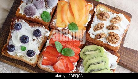 French Toast con formaggio a pasta morbida, fragole, kiwi, noci, ciliegie e mirtilli su un marrone di legno Foto Stock