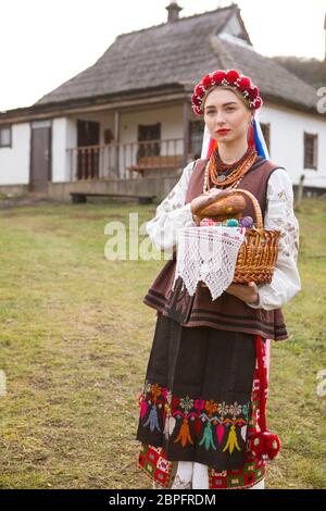 Bella ragazza in abito nazionale con Pasqua e uova in un cestino. Vacanze di Pasqua. In abiti antichi del 19 ° secolo. Con una corona e nastri. Agai Foto Stock