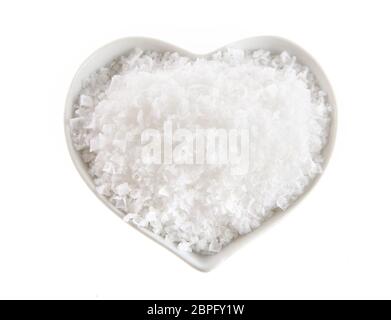 A forma di cuore ad una ciotola di Flor de Sal, un portoghese sale derivato dalla evaporazione di acqua di mare, visto dall'alto isolato su bianco Foto Stock