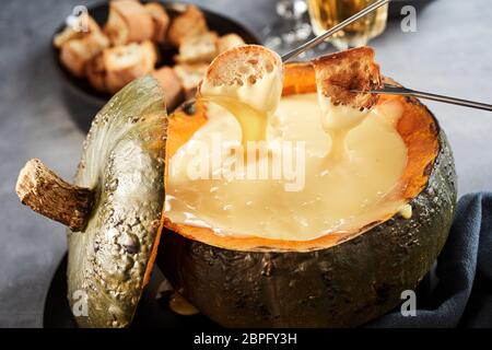 Gustosa fonduta di formaggio con forcelle di immersione con pane tostato rivestito in salsa di fuso servita in una zucca scavata in una vista ravvicinata adatto per advertis Foto Stock