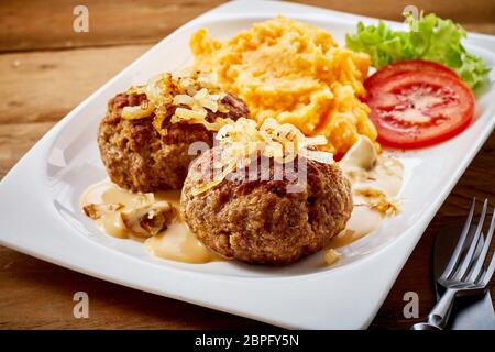 Speziato salato frikadellen tedesco o le polpette di carne condito con cipolle fritte e servito con una miscela di purea di patate e carote in un elevato angolo di visione per una m Foto Stock