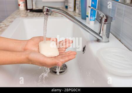 Il bambino tiene in mano il sapone in cui scorre l'acqua dal miscelatore Foto Stock