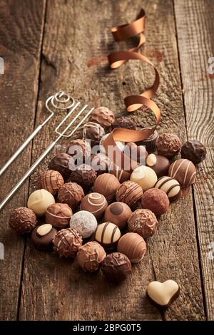 Grande assortimento di lusso fatti a mano praline di cioccolato su legno rustico con twirled festosa e a nastro singolo a forma di cuore ad bonbon al lato Foto Stock