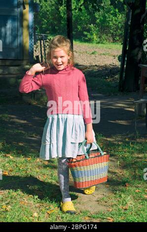 La bambina del villaggio sorride e tiene in mano un cestino di mele da giardino Foto Stock