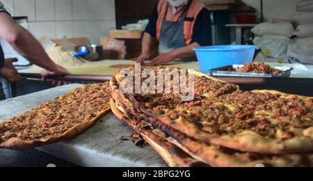 Primo piano di una pila di pitas turche di manzo macinato tradizionale messa su terra di marmo con due panettieri turchi maschi che riscaldano e preparano il cibo sul retro Foto Stock