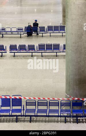 Passeggero solitario nel terminal aeroportuale vuoto durante una pandemia di coronavirus. Nastro protettivo rosso teso sulle sedie. Forte declino nel tra passeggeri Foto Stock