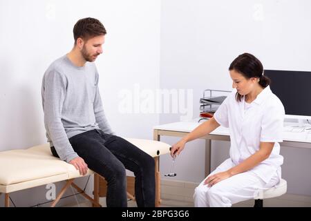 Giovani donne medico controllo riflessi del ginocchio del paziente di sesso maschile con martello Reflex Foto Stock