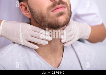 Medico la mano indossando i guanti di eseguire esame fisico palpazione della ghiandola tiroide Foto Stock