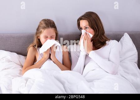 Madre e figlia soffrono di freddo soffia il naso con il fazzoletto sul letto Foto Stock