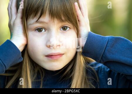 Ritratto di ragazza bambino sorpreso che tiene le mani alla sua testa all'aperto in estate. Scioccata femmina capretto in una calda giornata fuori. Foto Stock