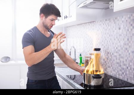 Scioccato Giovane guardando al recipiente di cottura di fuoco ardente sul fornello a induzione Foto Stock