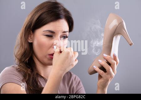 Close-up di una giovane donna Holding Stinky tacchi alti su sfondo grigio Foto Stock