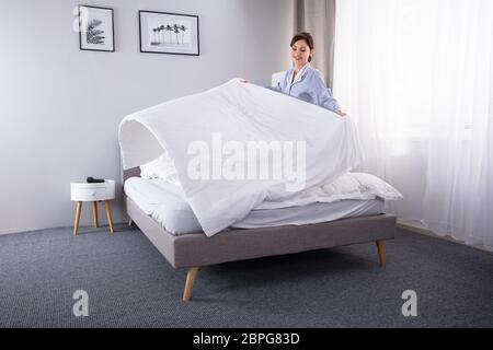 Sorridente Giovane Femmina la governante disponendo lenzuolo sul letto in camera di albergo Foto Stock