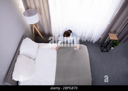 Donna sorridente governante rendendo letto in camera in hotel Foto Stock