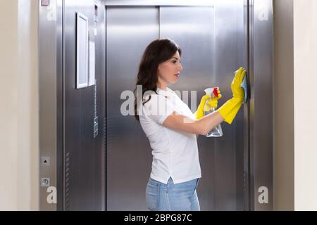 Vista laterale di un sorridente Giovane Femmina pulizia bidello di ascensore con Duster Foto Stock