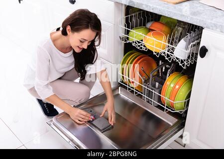 Felice giovane donna mettendo il sapone compressa nella casella di lavastoviglie Foto Stock