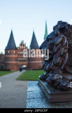 Holstentor a Lübeck con la statua del leone in primo piano, patrimonio dell'umanità dell'UNESCO, simbolo di stile gotico, ornamenti storici del paesaggio urbano restaurato in mattoni P. Foto Stock
