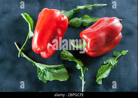 Res peperoni e foglie di rucola su un nero sfondo rustico Foto Stock