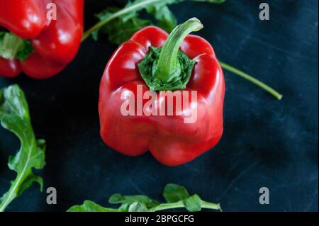 Res peperoni e foglie di rucola su un nero sfondo rustico Foto Stock