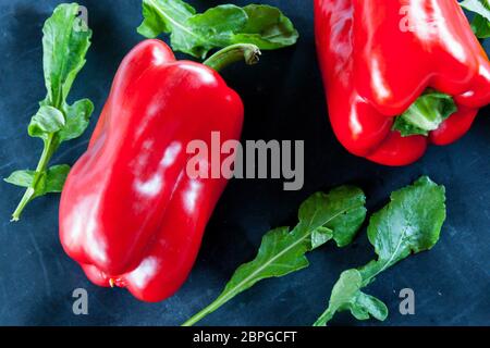 Res peperoni e foglie di rucola su un nero sfondo rustico Foto Stock