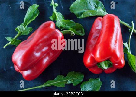 Res peperoni e foglie di rucola su un nero sfondo rustico Foto Stock