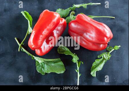 Res peperoni e foglie di rucola su un nero sfondo rustico Foto Stock