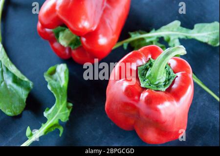 Res peperoni e foglie di rucola su un nero sfondo rustico Foto Stock