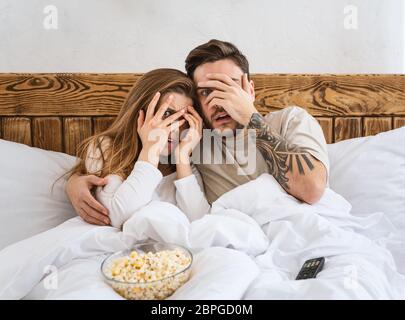 Concetto di film serale. Ragazzo e ragazza copre le facce con le mani, seduto a letto Foto Stock