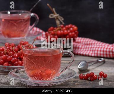 Hot viburnum tè in una coppa trasparente con una maniglia ed un piattino sul grigio di un tavolo di legno, accanto ai frutti di bosco freschi Foto Stock