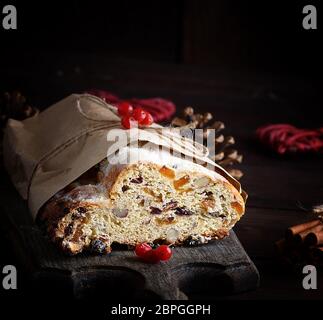 Europea tradizionale Stollen con torta di noci e frutta candita avvolto in un marrone pezzo di carta su una tavola di legno Foto Stock